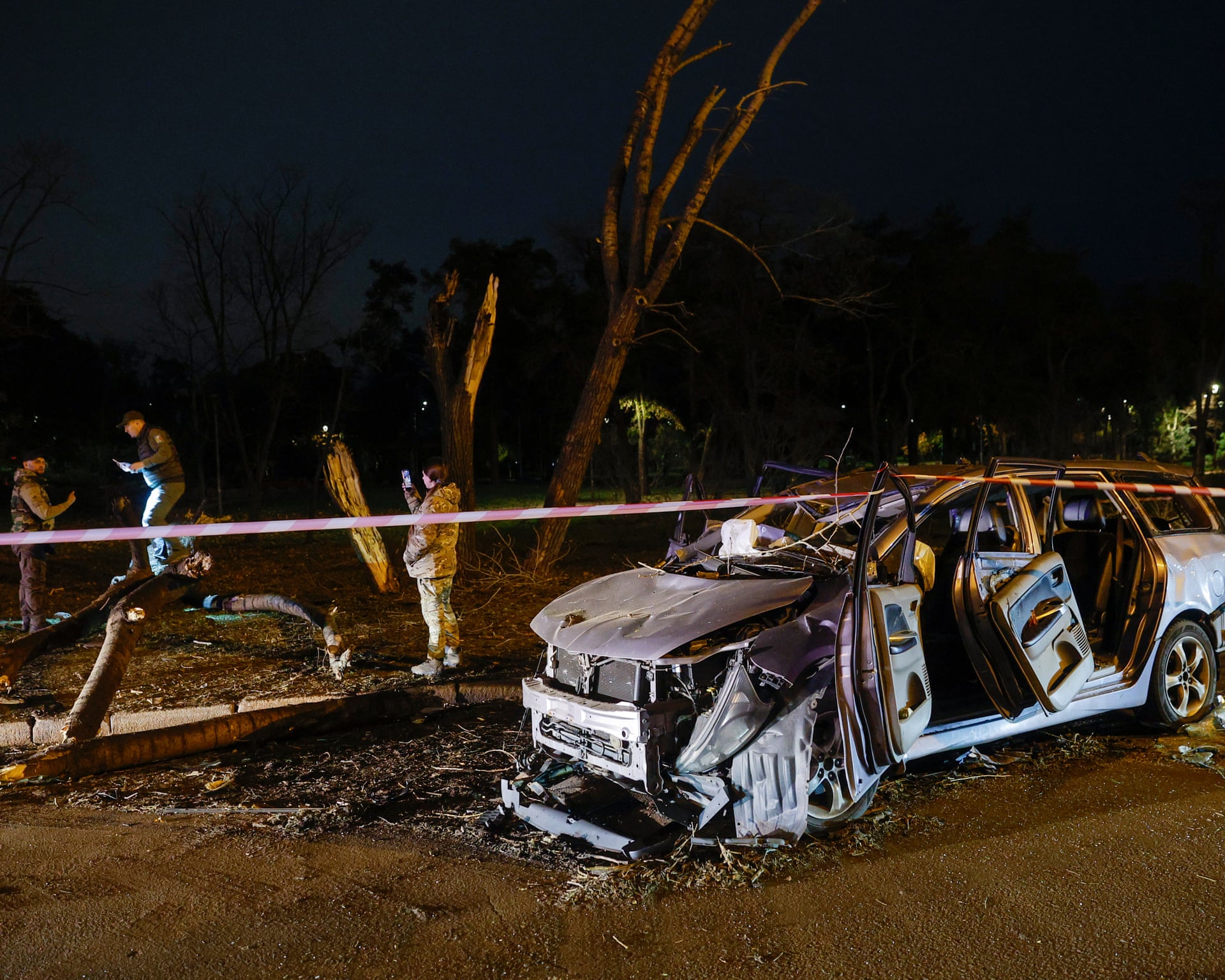 Investigators inspect a wrecked car at night at the site of a Russian missile strike in Kyiv.